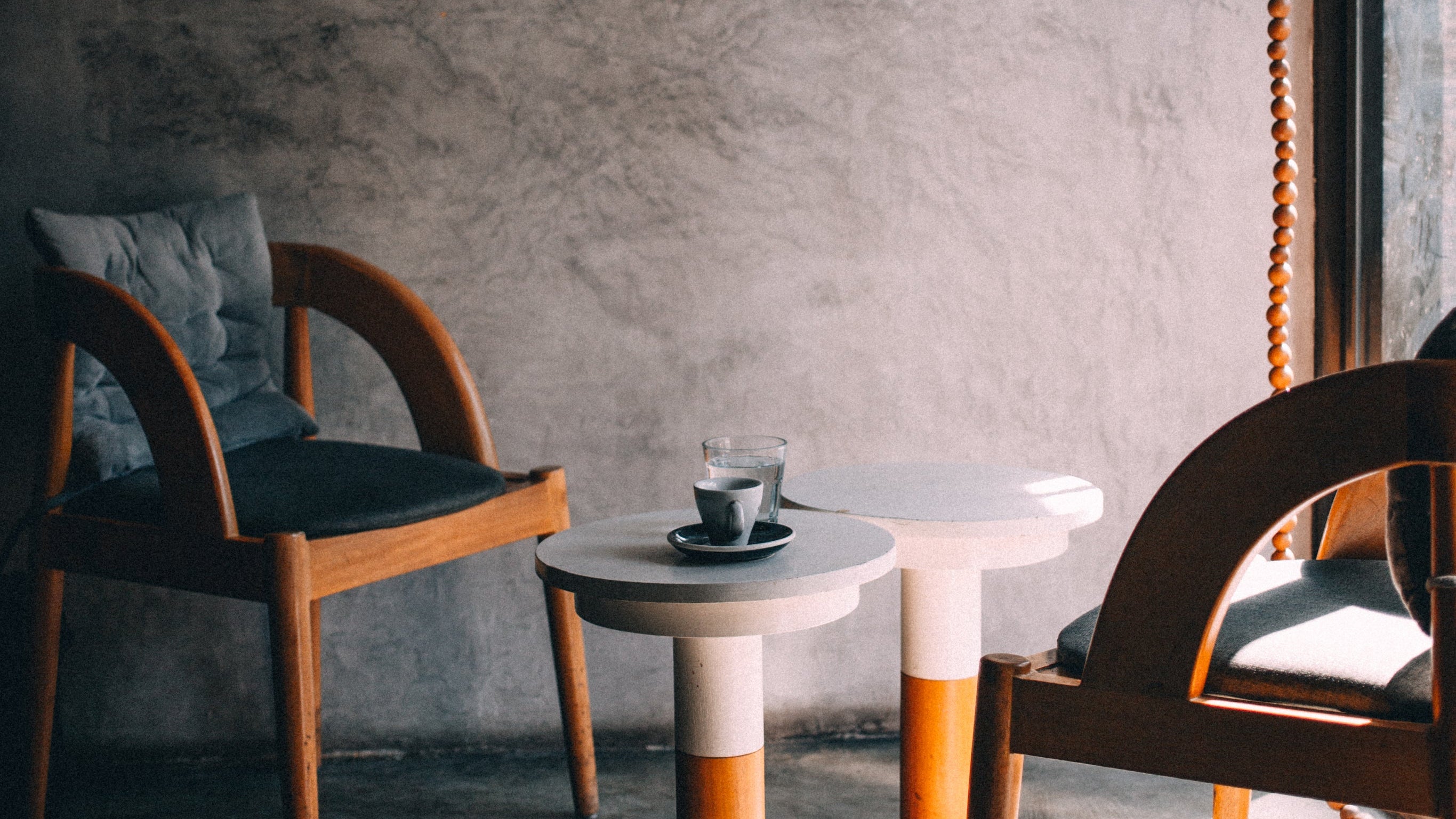 Two wooden chairs with a small round table against a gray wall.